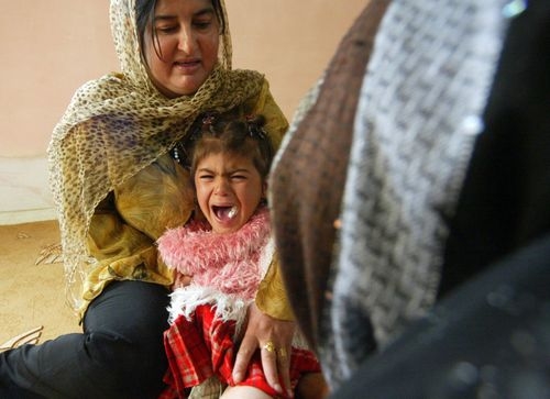 baby girl screaming in pain crying from experience of female genital mutilation, with older woman holding onto her