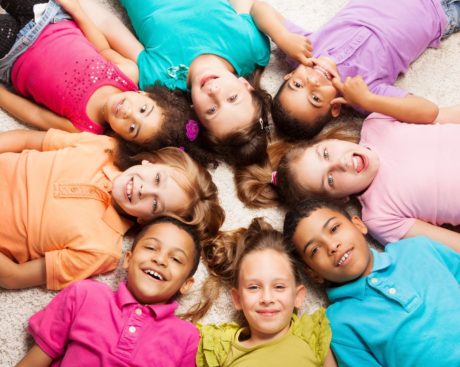 group of children laying on floor in a circle head to head smiling in unity