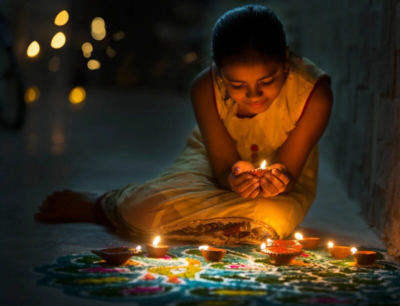 young girl holding candle ready to place into a festival of lights on ground in front of her