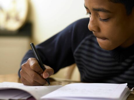 young boy about twelve writing in notebook sitting at desk