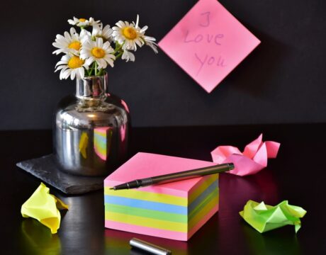 vase of daisies with pink wrapper box of candy and love note on pink sticky on background wall 
