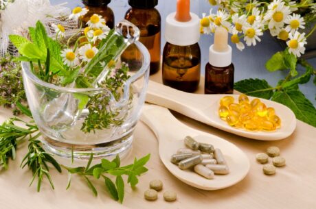 table filled with an array of oils in both vials and pill forms with glass bowl of flowers