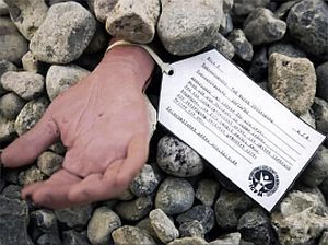 a woman's hand reaching out of a pile of rocks after a stoning