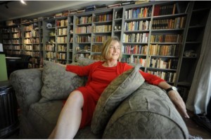 katherine govier wearing red dress sitting in a library with floor to ceiling books