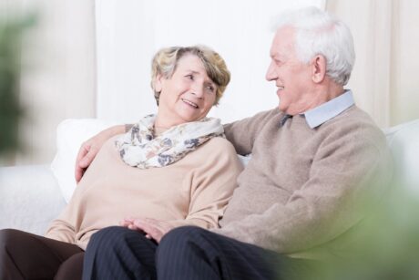 senior couple sitting on green sofa smiling at each other showing a happy and healthy lifestyle