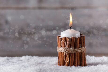 holiday candle wrapped in cinnamon sticks tied with hemp rope sitting on snow covered surface