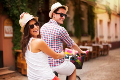 happy smiling couple on a bicycle built for two wearing sunglasses and white hats showing to be a perfect couple