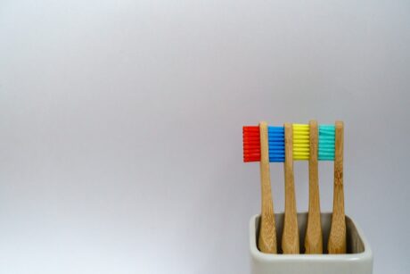four toothbrushes in different colors in white cup sitting on plain grey background in photo
