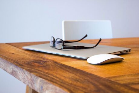 woman's eyeglasses sitting on top of laptop that site on oak desk with white chair showing signs of a woman's office