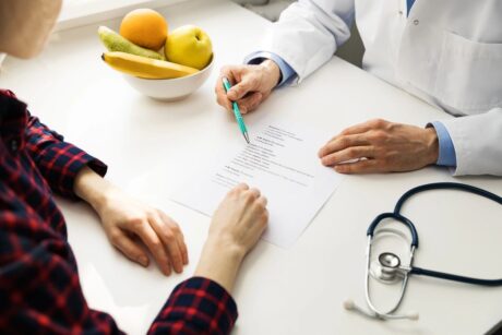 woman sitting with doctor reviewing test results discussing lifestyle as a stethoscope and bowl of fruit are on desk