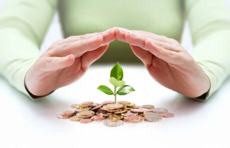 woman's hands folded on top of tiny plant growing through a pile of coins exhibiting care for money