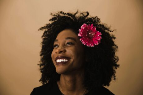 beautiful black woman smiling with pink flower set into her short wavy hairdo