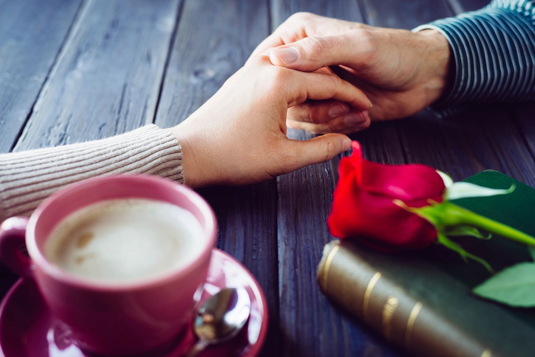 couple holding hands with coffee, book and a rose on table showing intimacy