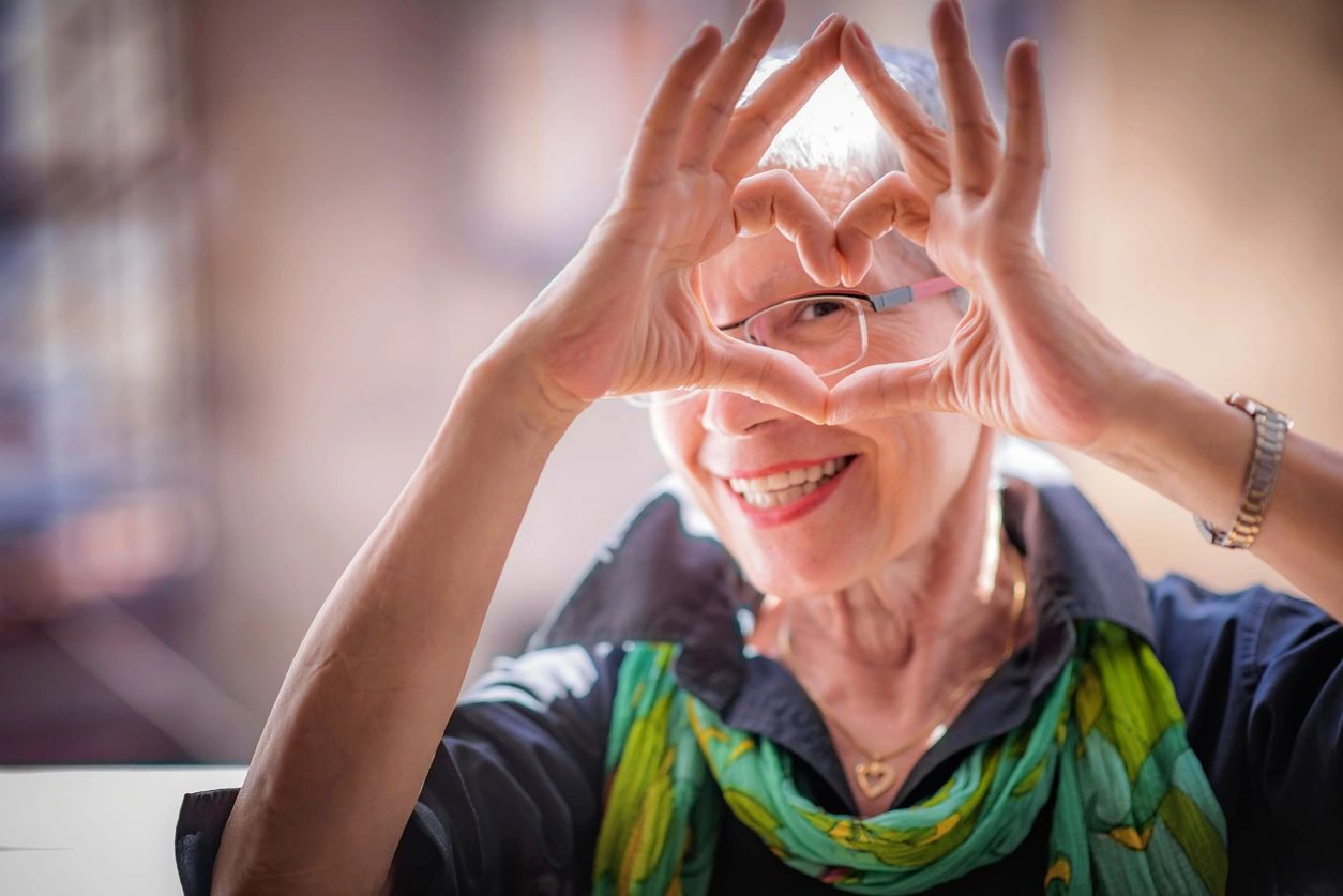 senior smiling woman holding hands together with fingers forming a heart shape 