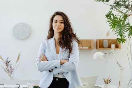 women wearing business jacket crossing arms leaning on desk showing empowerment