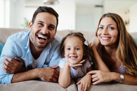 smiling couple with daughter all showing beautiful teeth