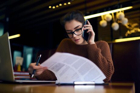 woman at desk studying paperwork while on cell wearing eyeglasses looking very professional