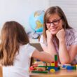 woman leaning on desk working with activity blocks with a girl