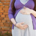 pregnant woman wearing purple sweater and white dress